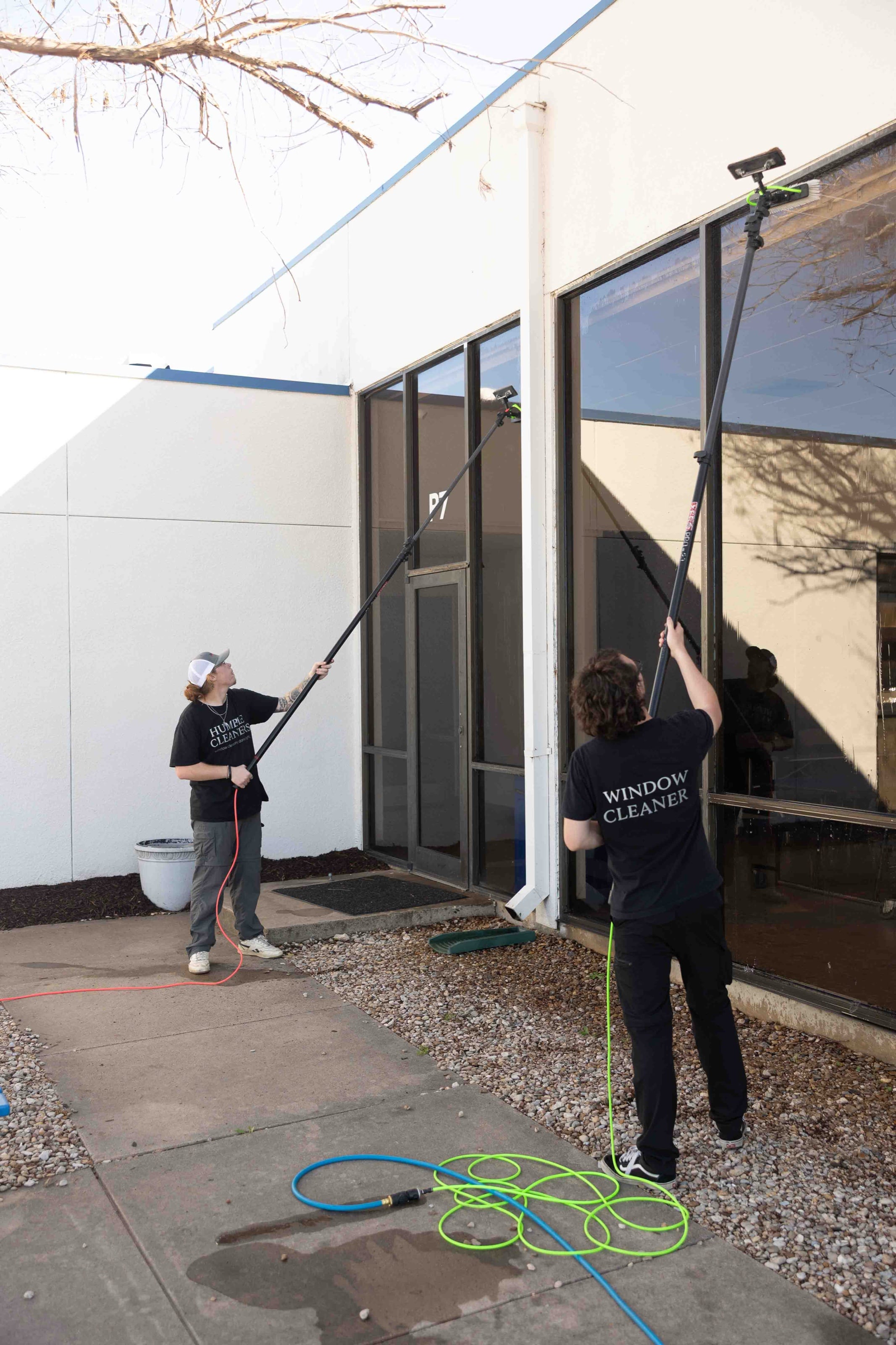 Two Humble Cleaners crew members running water-fed poles up tall glass