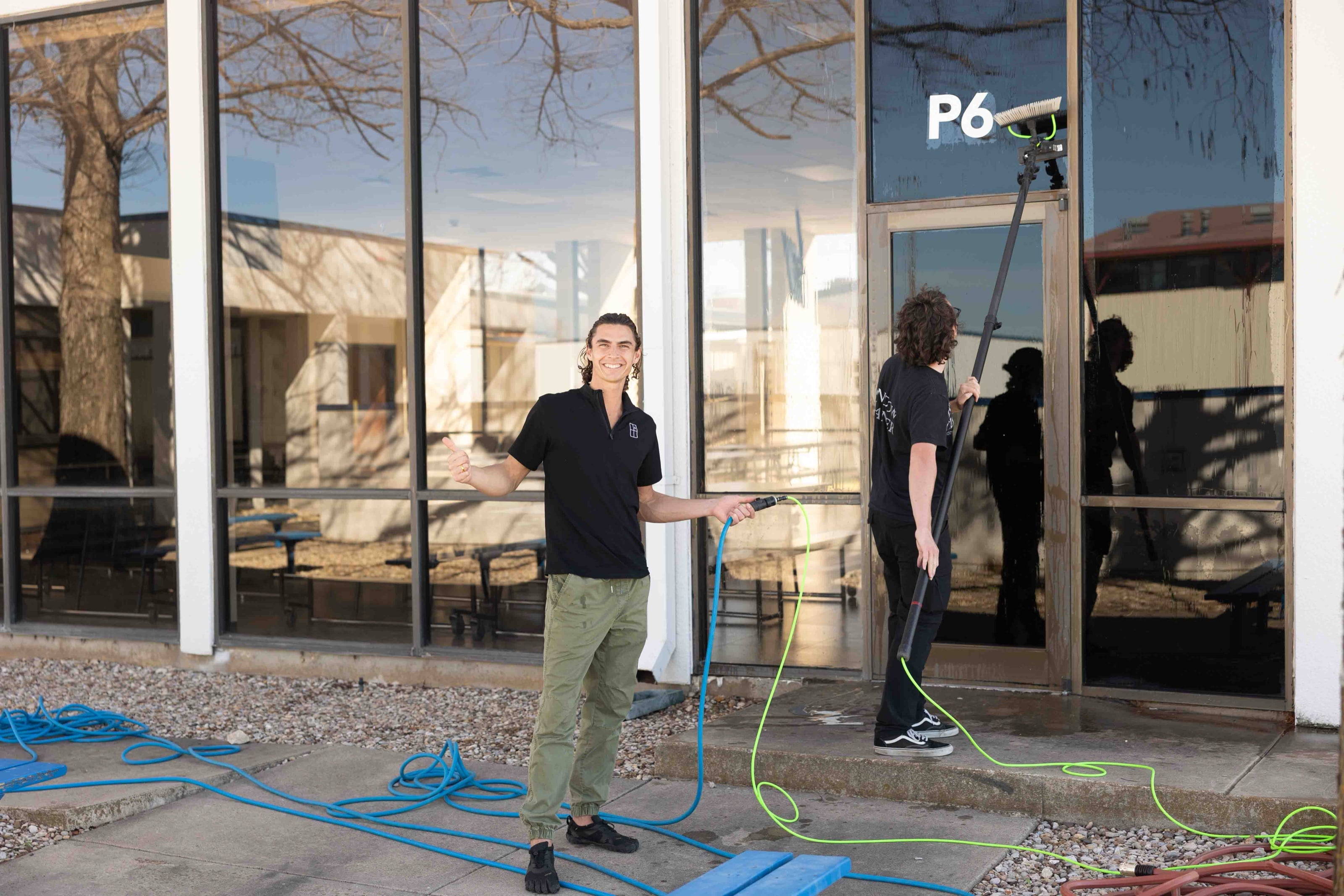 A Humble Cleaners crew member giving a thumbs-up while washing glass with the water-fed pole